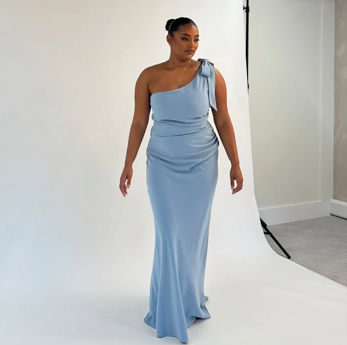 Woman wearing a light blue one-shoulder bridesmaid gown against a white background