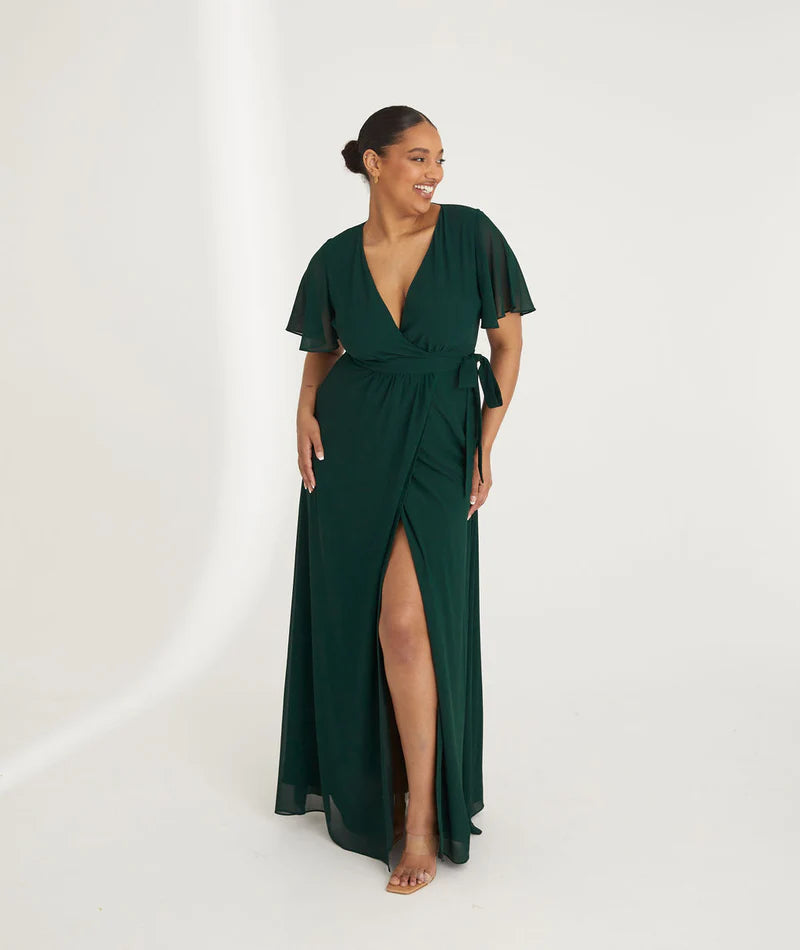 Woman wearing an emerald green chiffon gown with ruffled shoulders on a white background