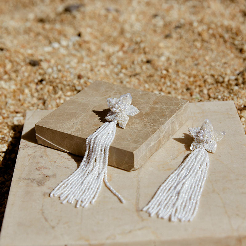 Image of long star shaped ivory beaded tassel earrings against a sandstone backdrop.