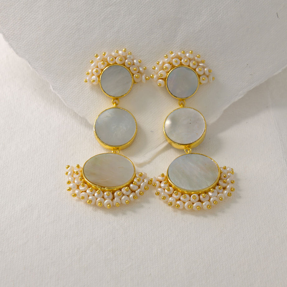 Pair of statement mother of pearl earrings on a gold stand against a light grey background