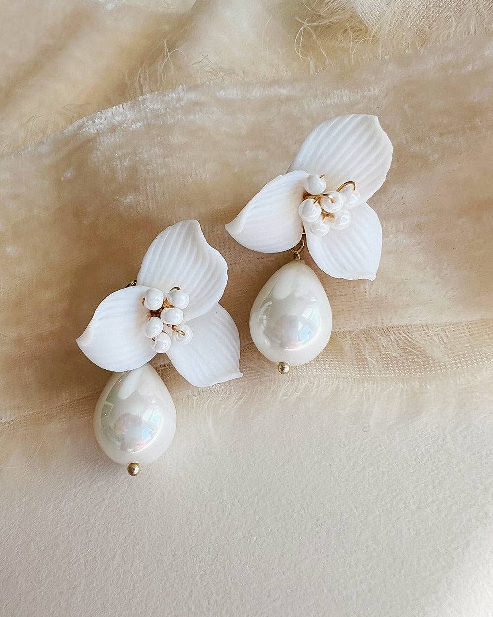 Make a statement of timeless sophistication on your wedding day with the Laurel Pearl Drop Earrings — a striking blend of modern design and classic beauty. Thoughtfully handcrafted, these earrings feature delicate ivory clay flowers paired with a luminous pear-shaped pearl that adds effortless refinement to any bridal or special occasion look.