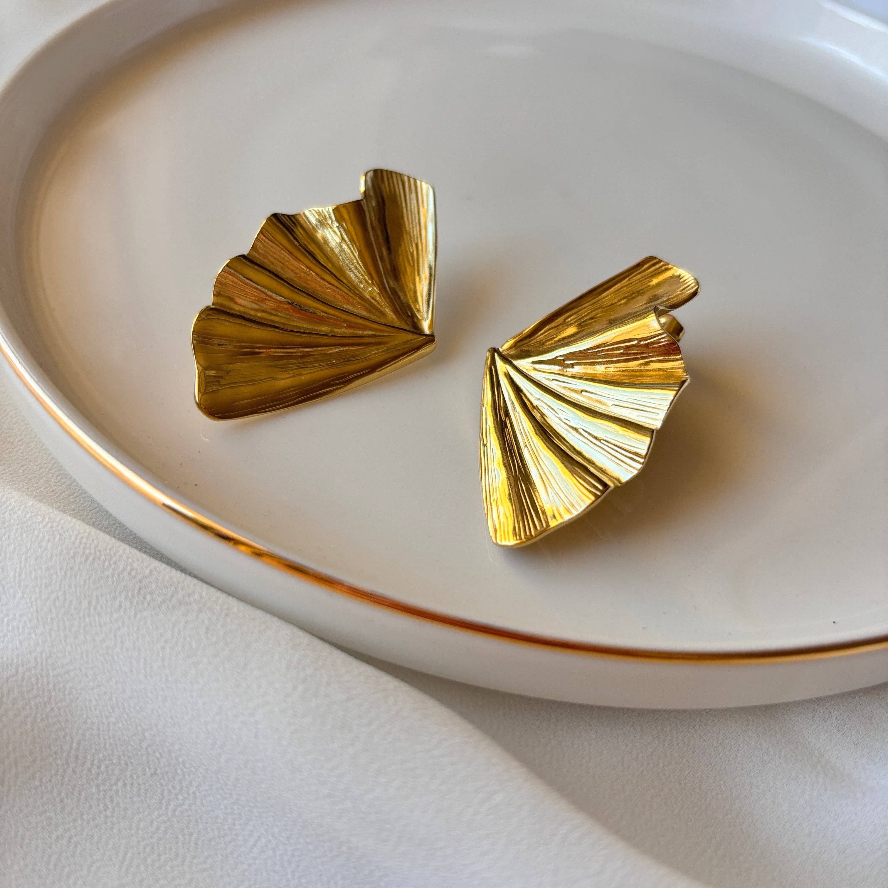 Gold fan-shaped earrings on a white plate