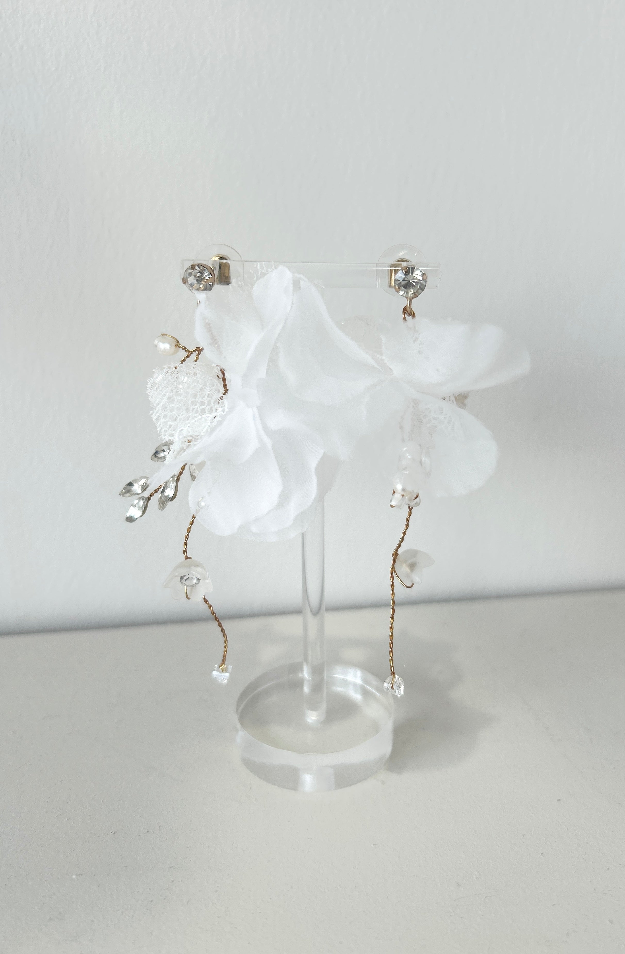 Pair of bridal earrings with white floral and crystal drop on a white background
