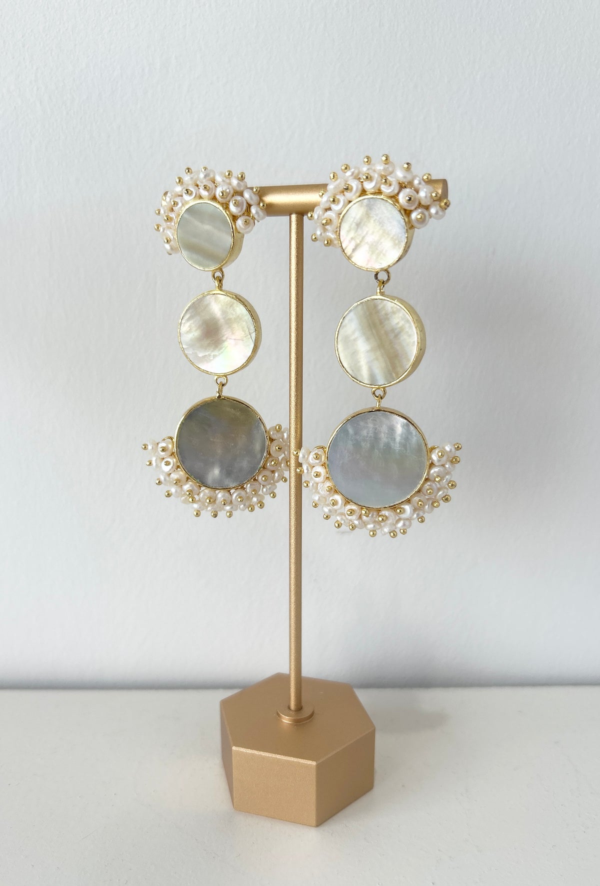 Pair of statement mother of pearl earrings on a gold stand against a light grey background