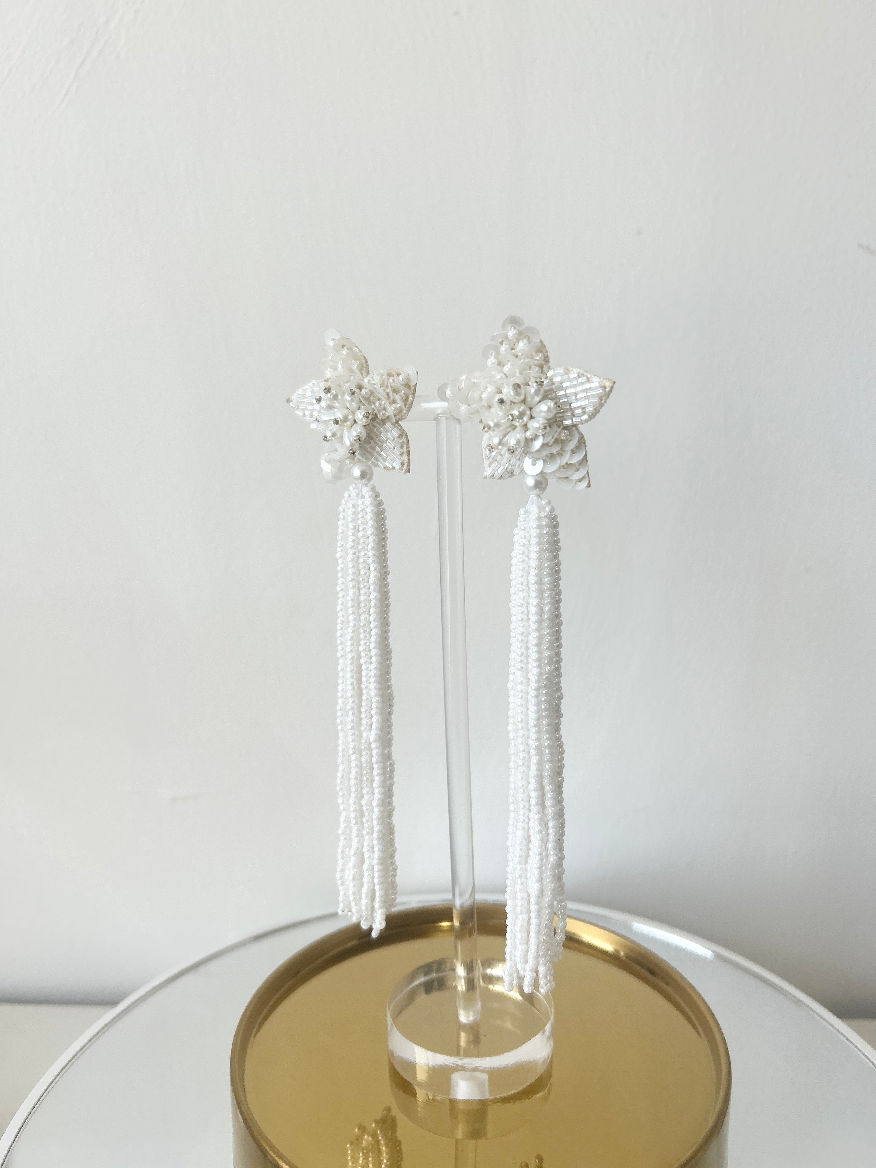 Image of long star shaped ivory beaded tassel earrings against a white backdrop.