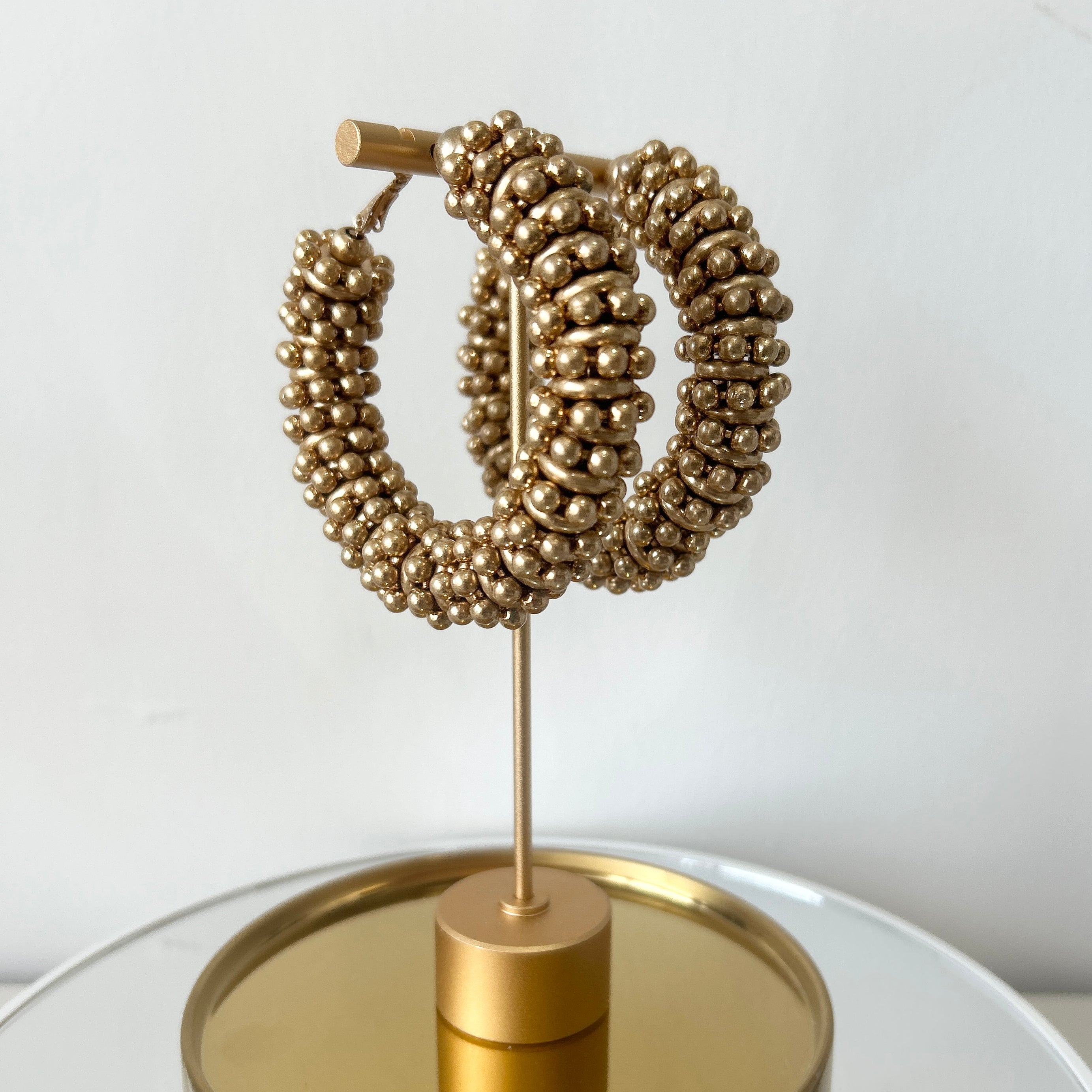 Gold hoop earrings on a stand with a plain background