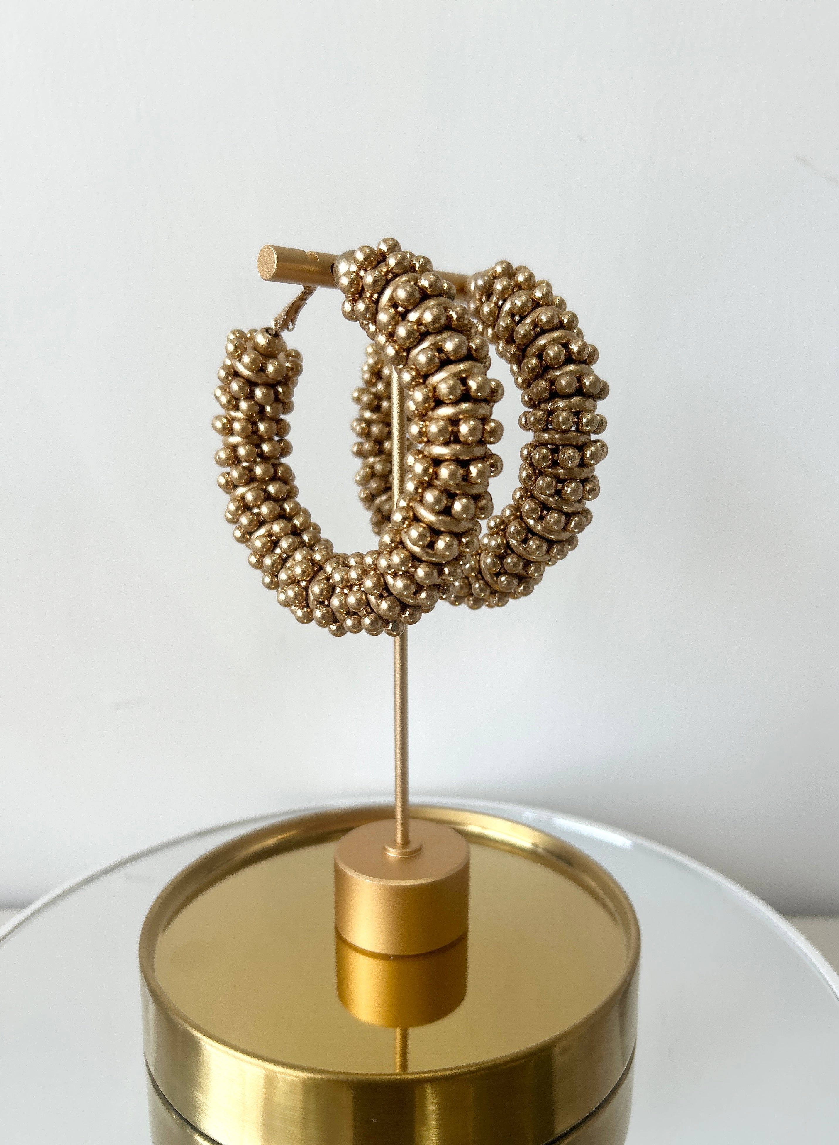 Gold hoop earrings on a stand with a plain background