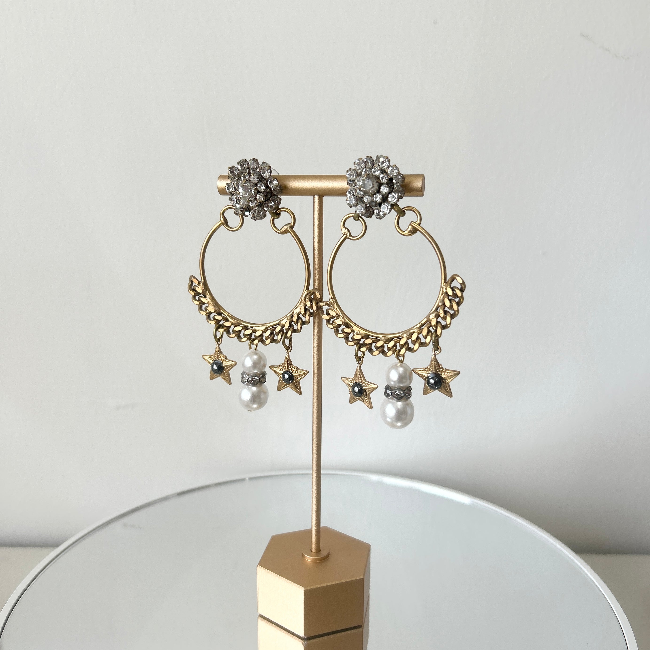 A pair of earrings featuring a gold-colored antique chain circlet with a Swarovski crystal cluster at the top, adorned with pearl, crystal, and starlet charms.