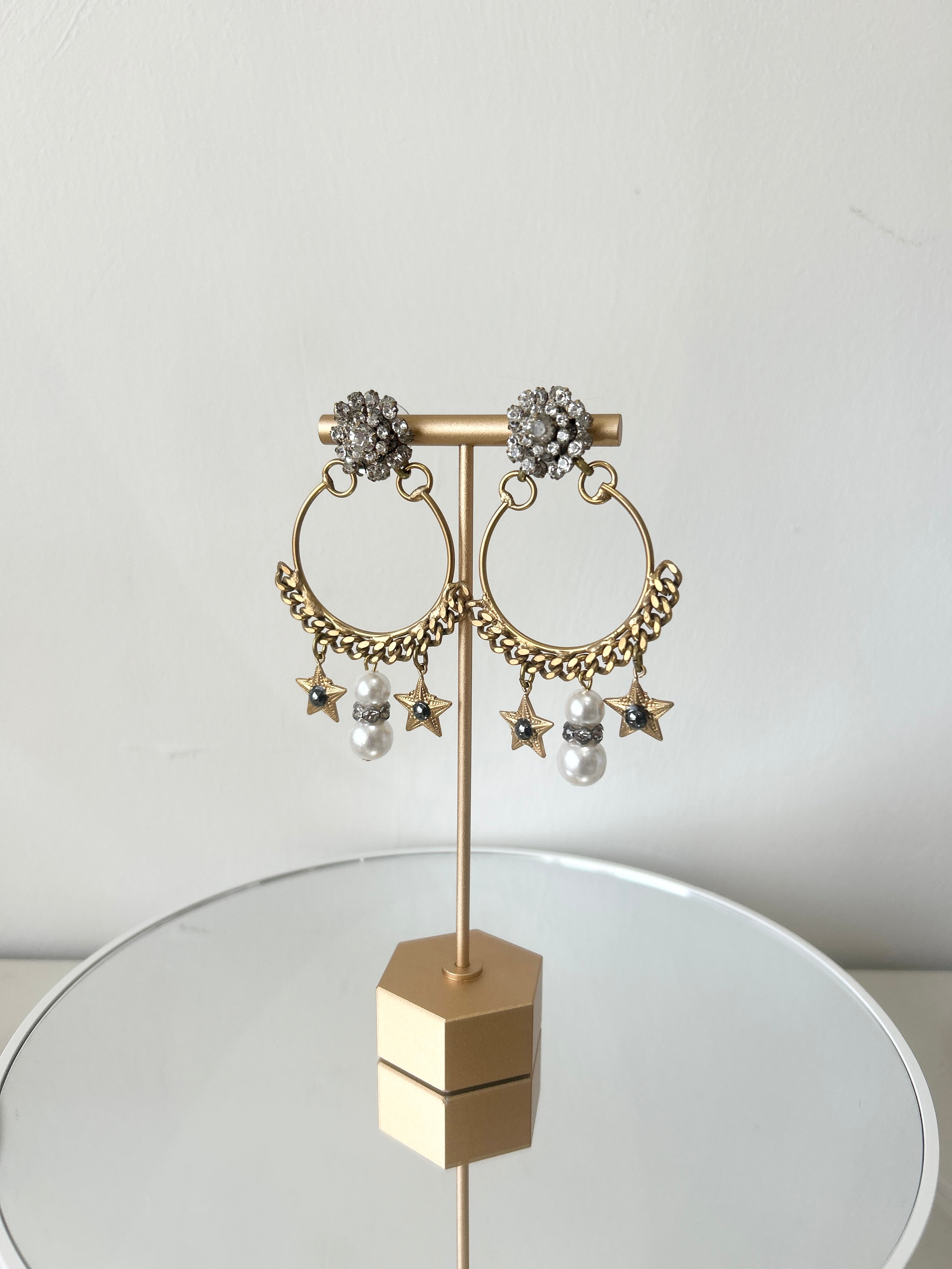 A pair of earrings featuring a gold-colored antique chain circlet with a Swarovski crystal cluster at the top, adorned with pearl, crystal, and starlet charms.