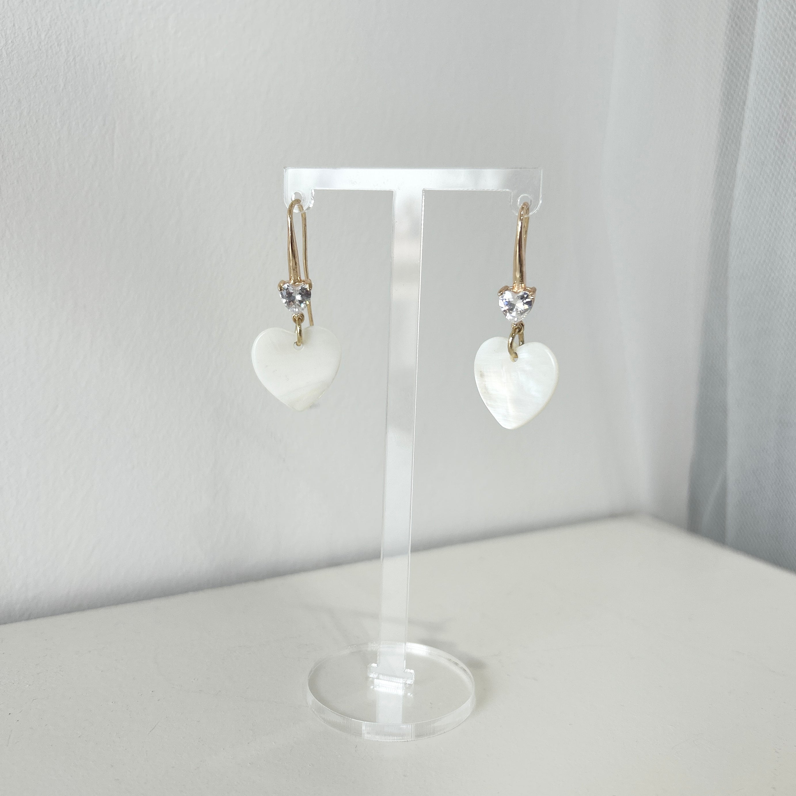 Mother of pearl heart-shaped earrings on a clear stand against a white background