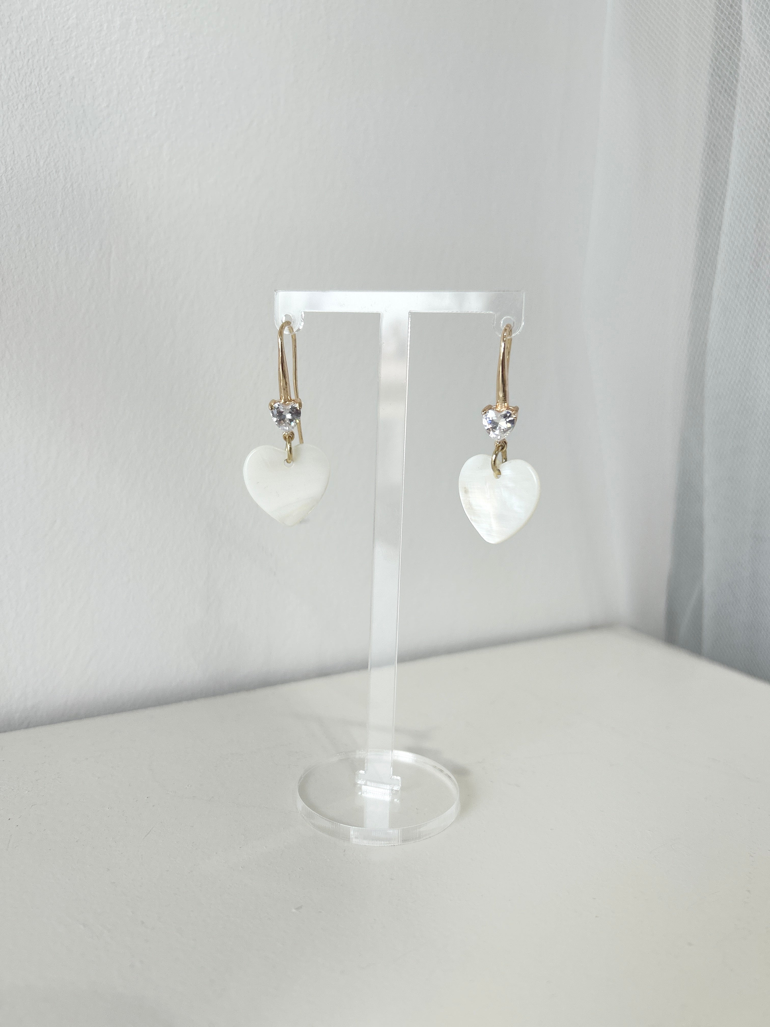 Mother of pearl heart-shaped earrings on a clear stand against a white background
