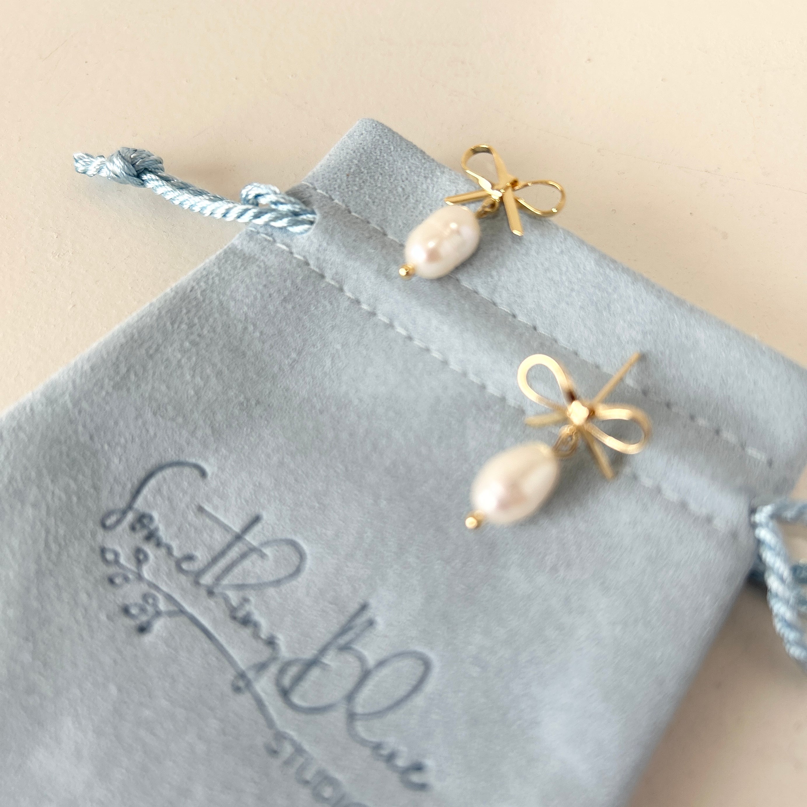 Pair of pearl earrings on a velvet jewellery pouch with 'Something Blue Studio' branding.