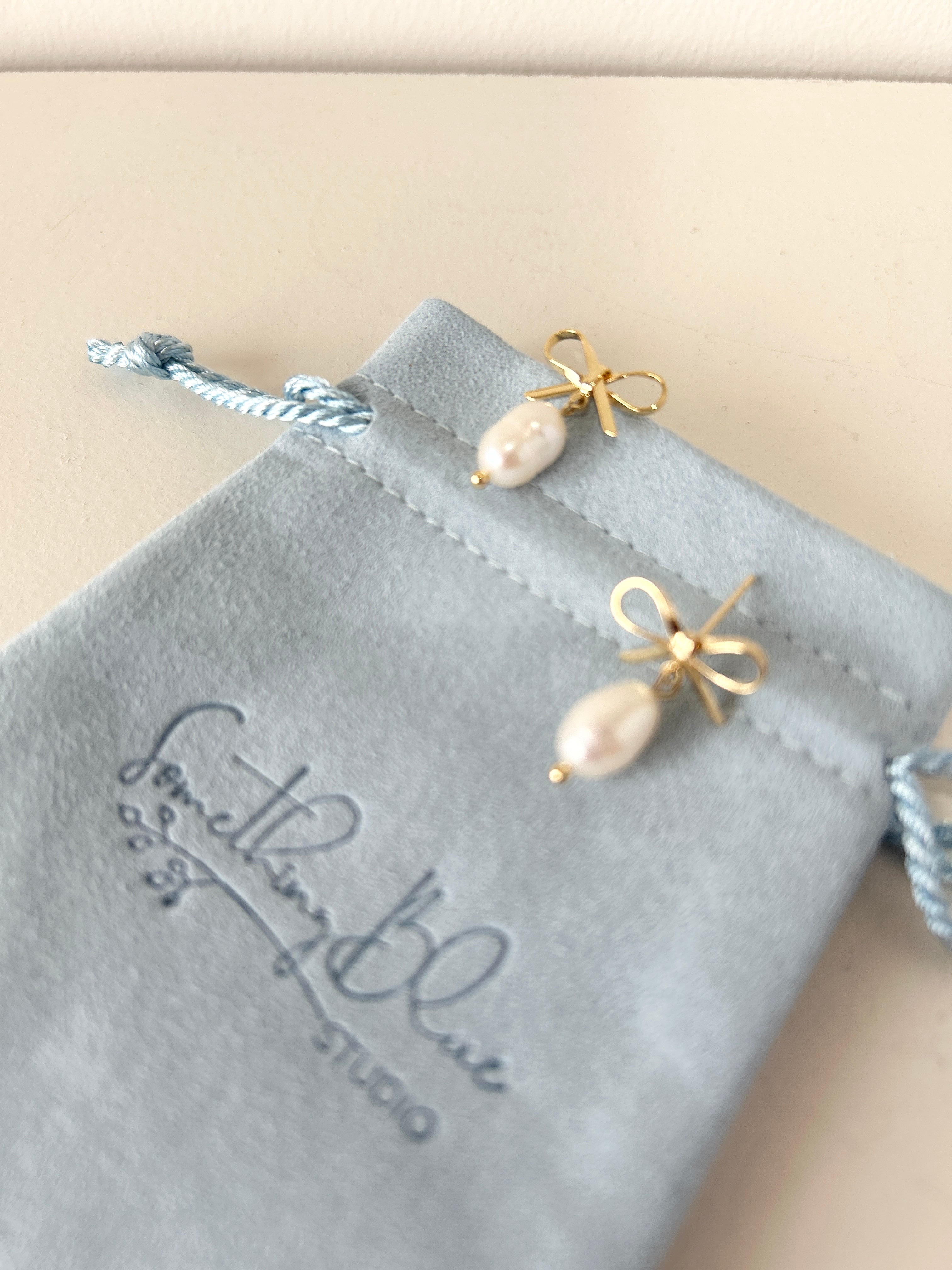 Pair of pearl earrings on a velvet jewellery pouch with 'Something Blue Studio' branding.