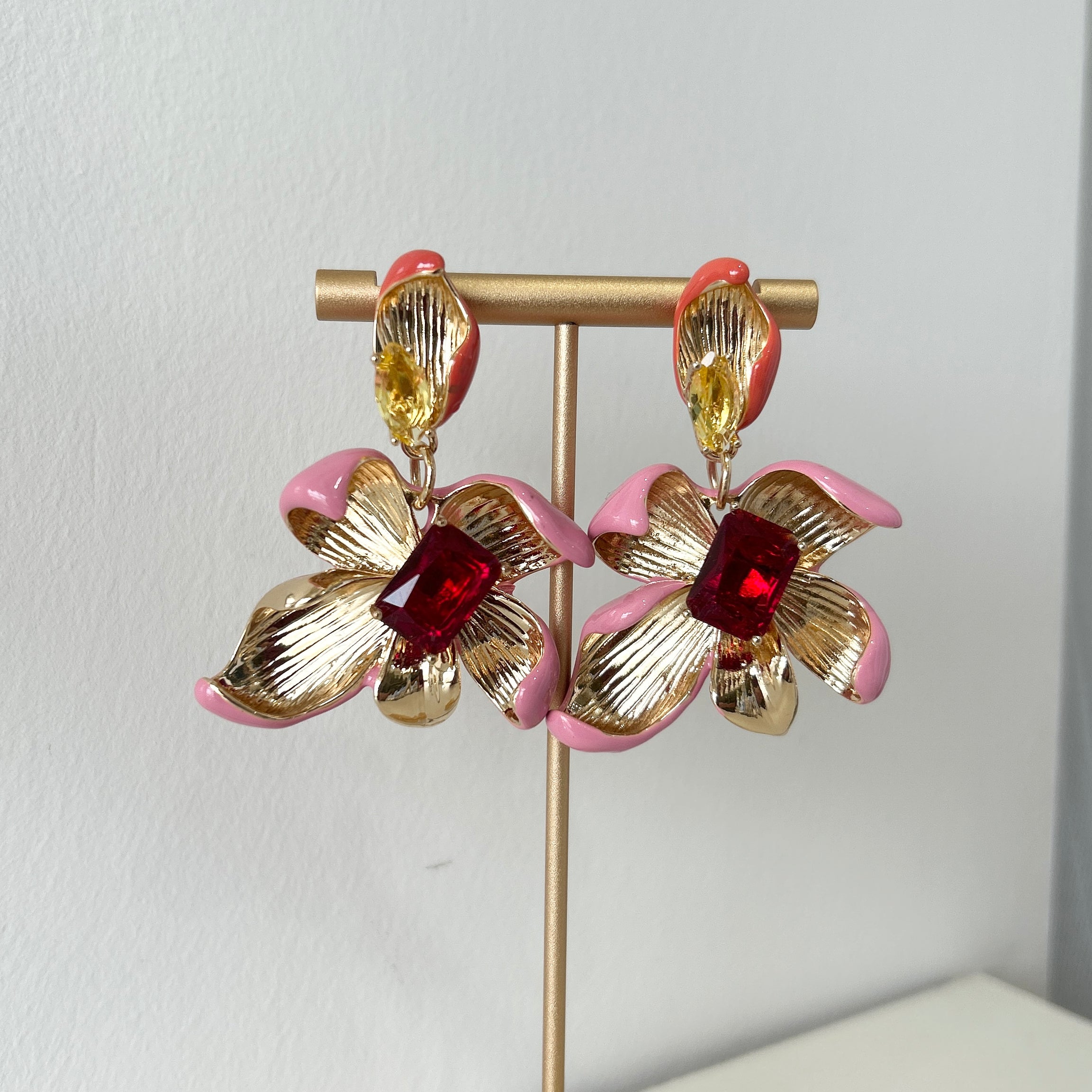 Pair of gold and pink floral earrings on a stand against a white background