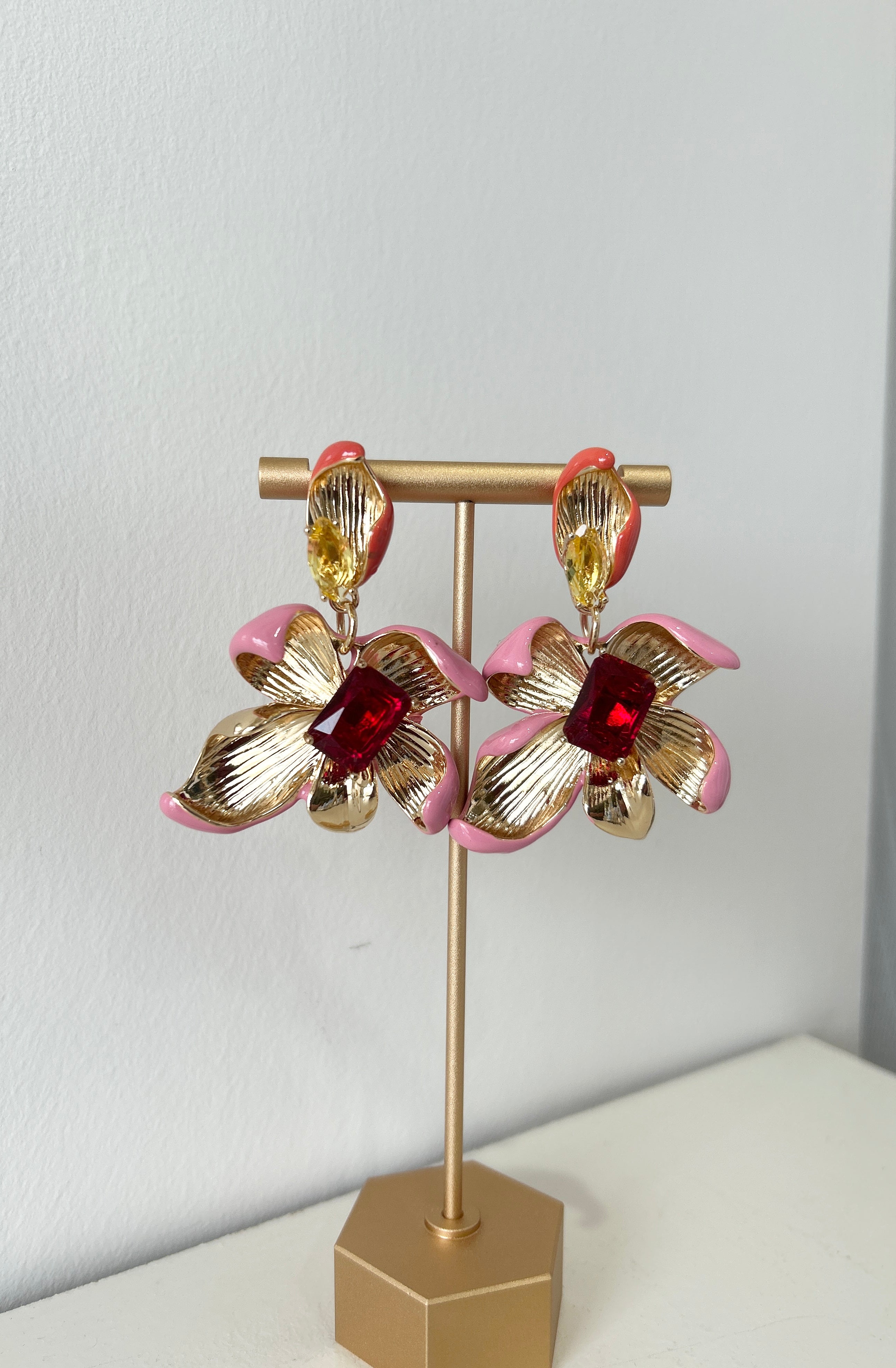 Pair of gold and pink floral earrings on a stand against a white background