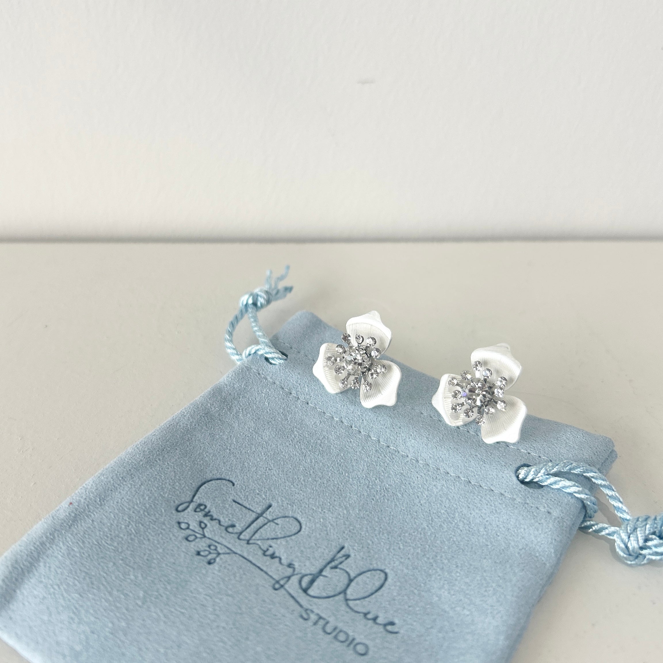 Floral earrings on a 'Something Blue Studio' branded jewelry pouch.
