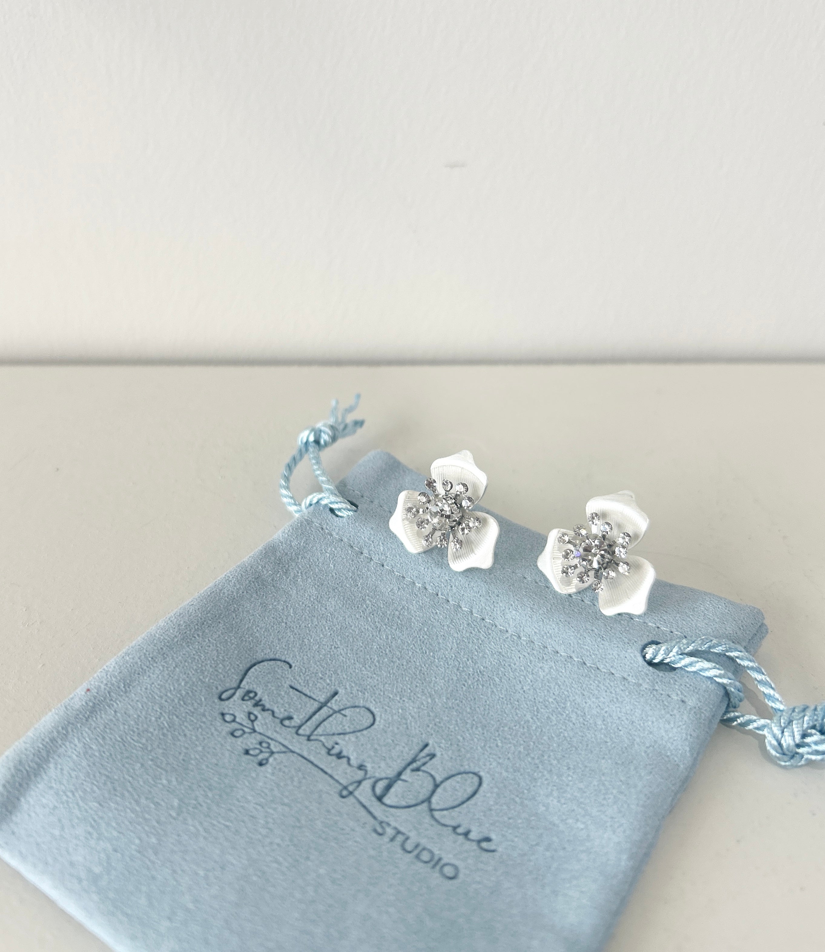 Floral earrings on a 'Something Blue Studio' branded jewelry pouch.