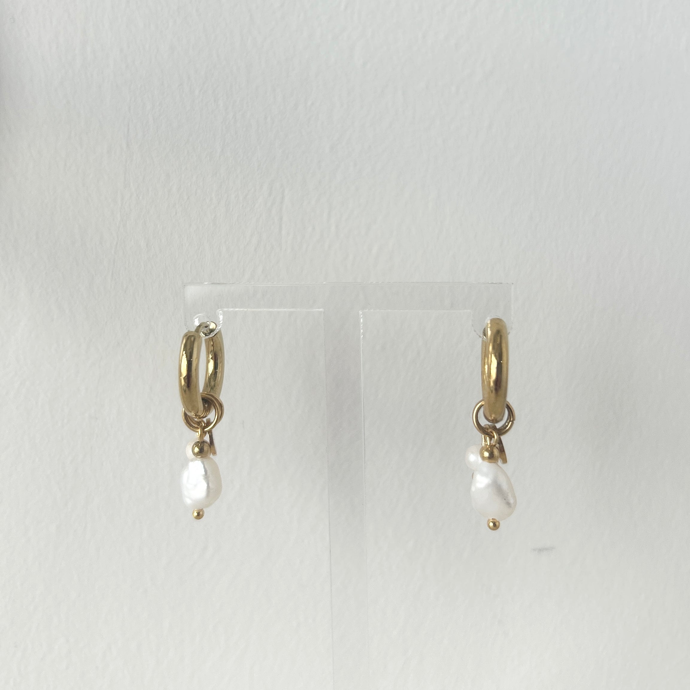 Gold earrings with pearl drops on a clear stand against a white background