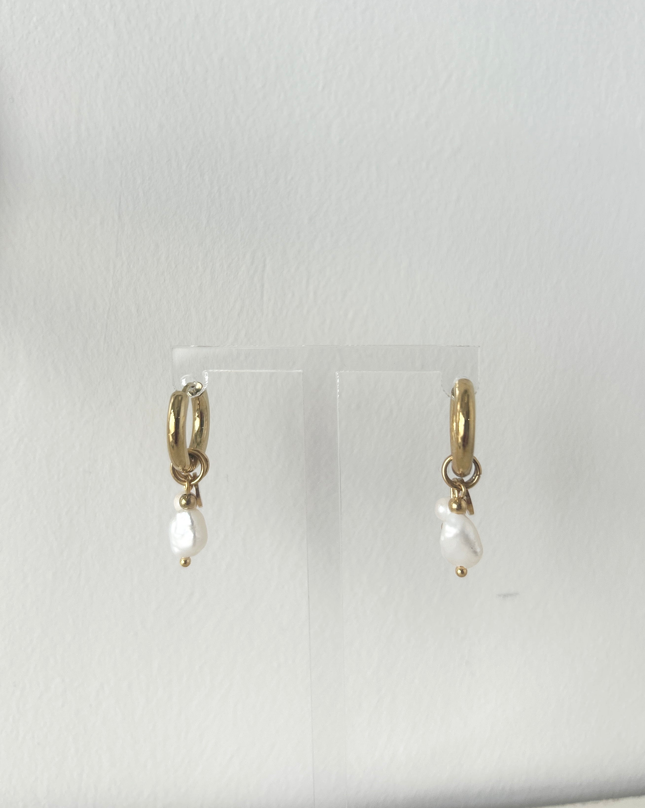 Gold earrings with pearl drops on a clear stand against a white background
