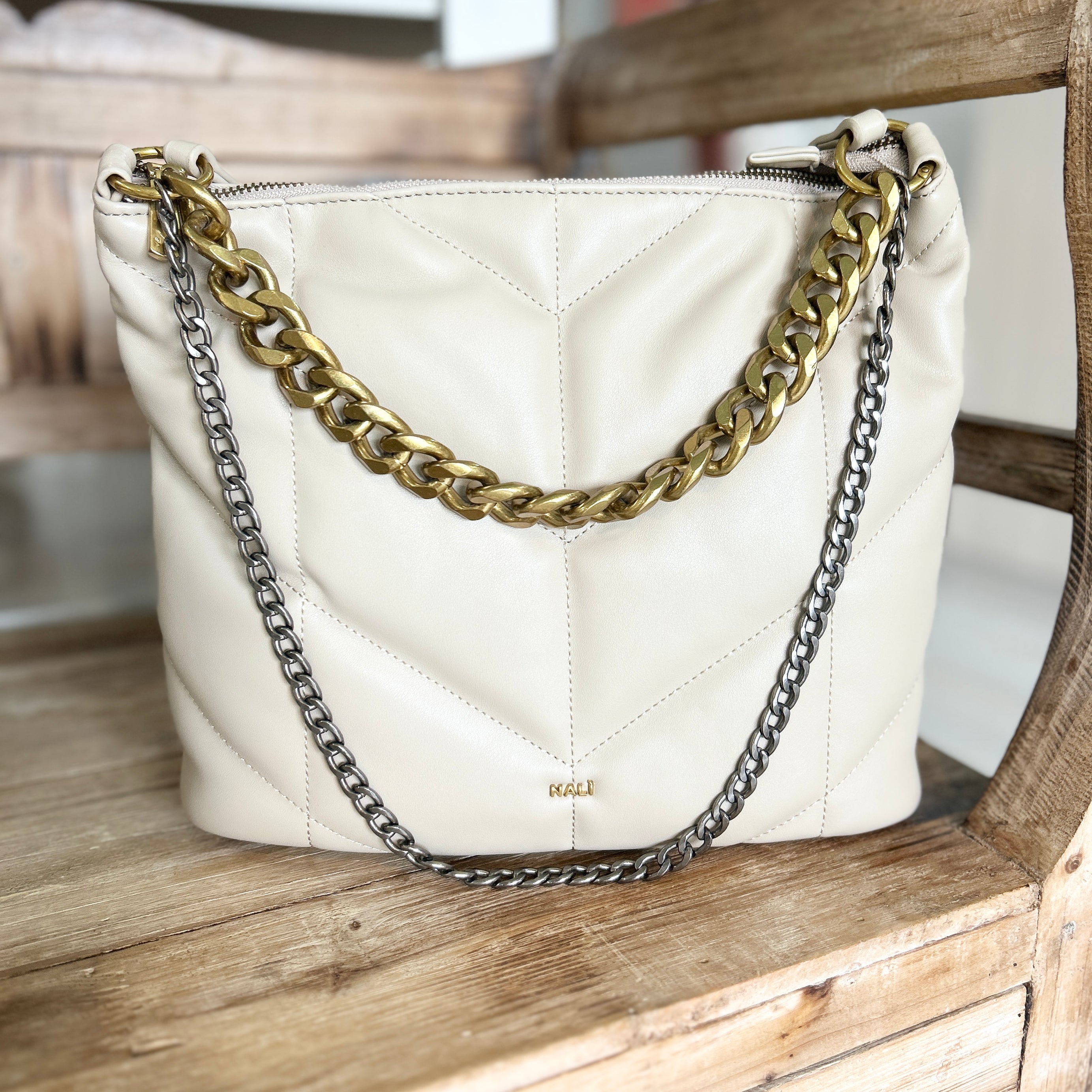 Beige handbag with chunky gold and silver chain detail on a wooden surface