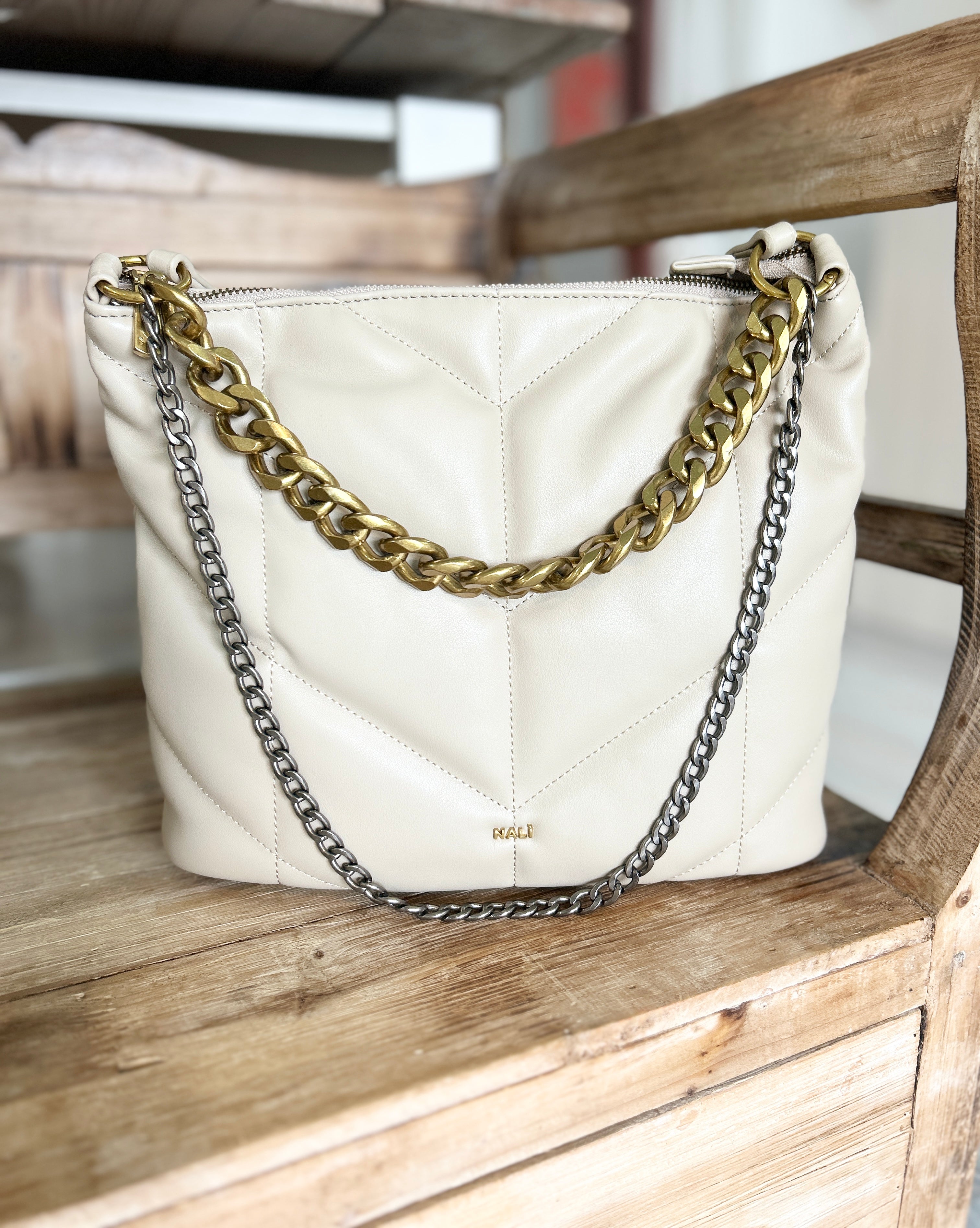 Beige handbag with chunky gold and silver chain detail on a wooden surface