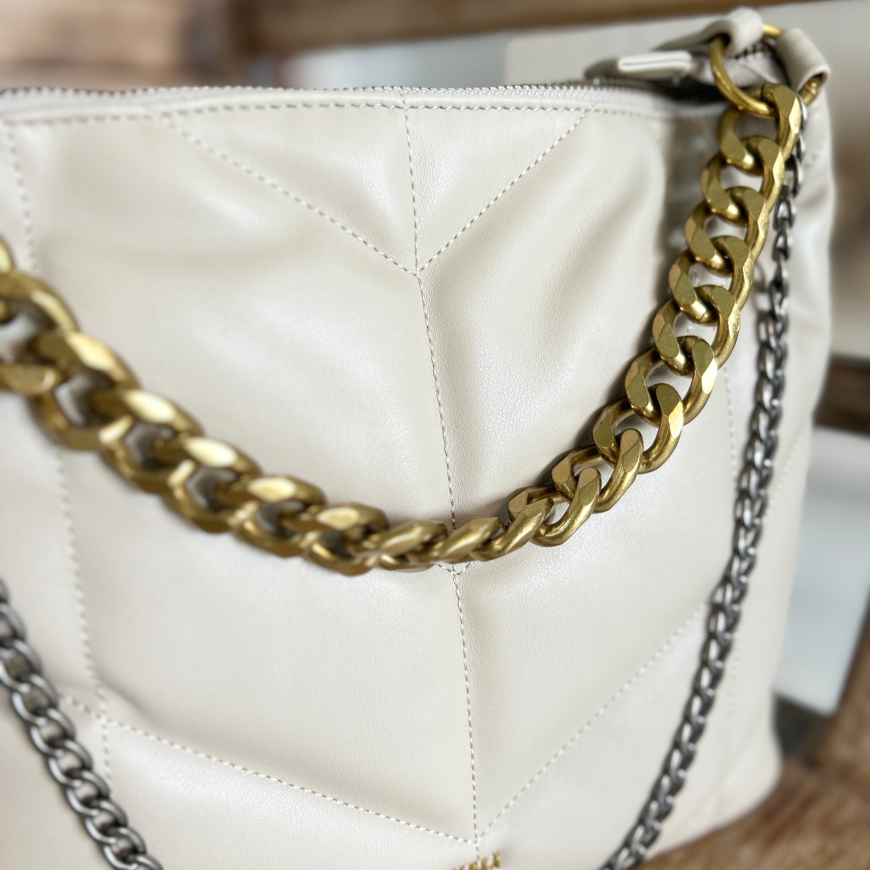 Beige handbag with chunky gold and silver chain detail on a wooden surface