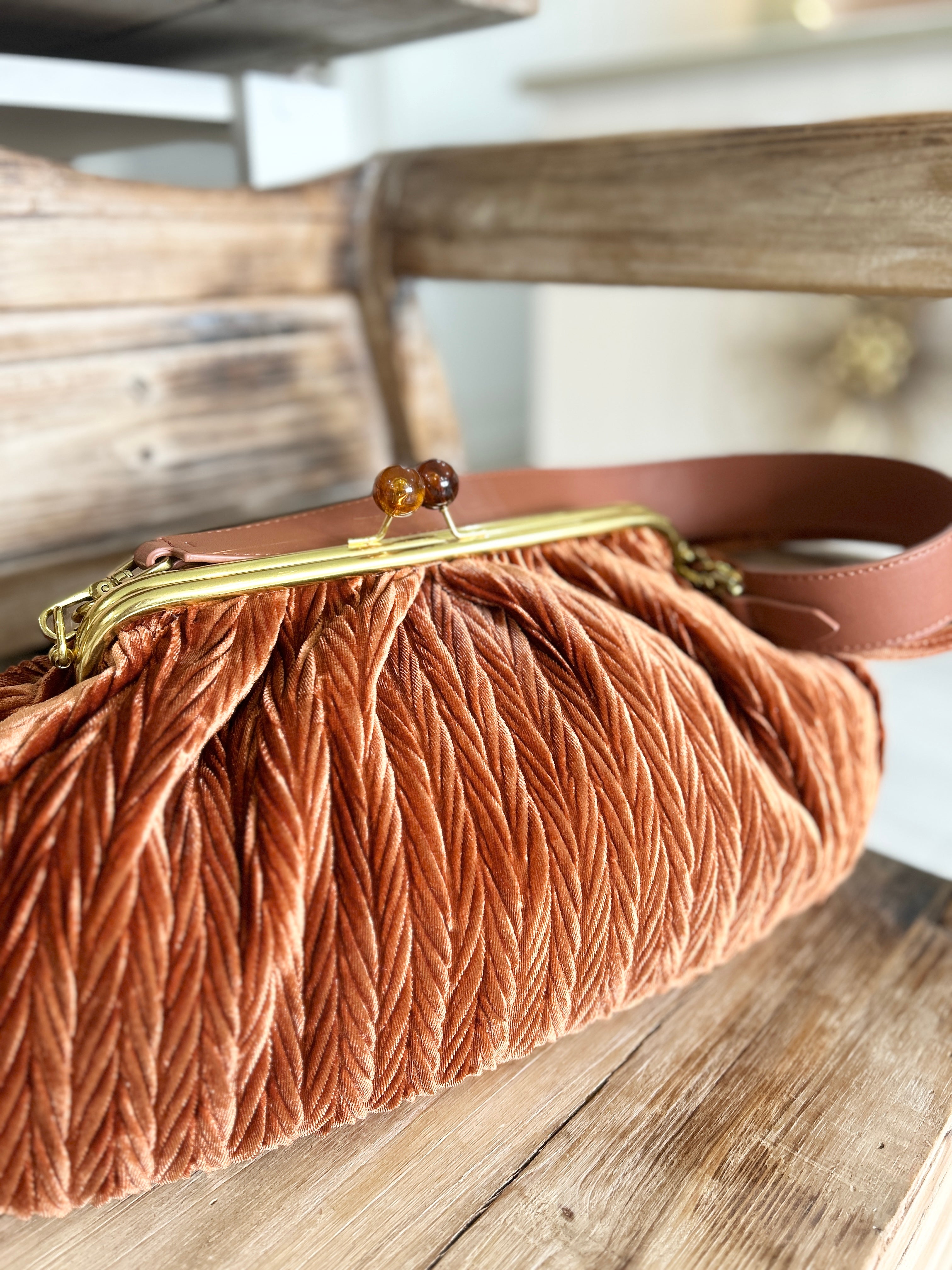 Brown vintage style brown velvet handbag with a gold snap clasp on a wooden surface