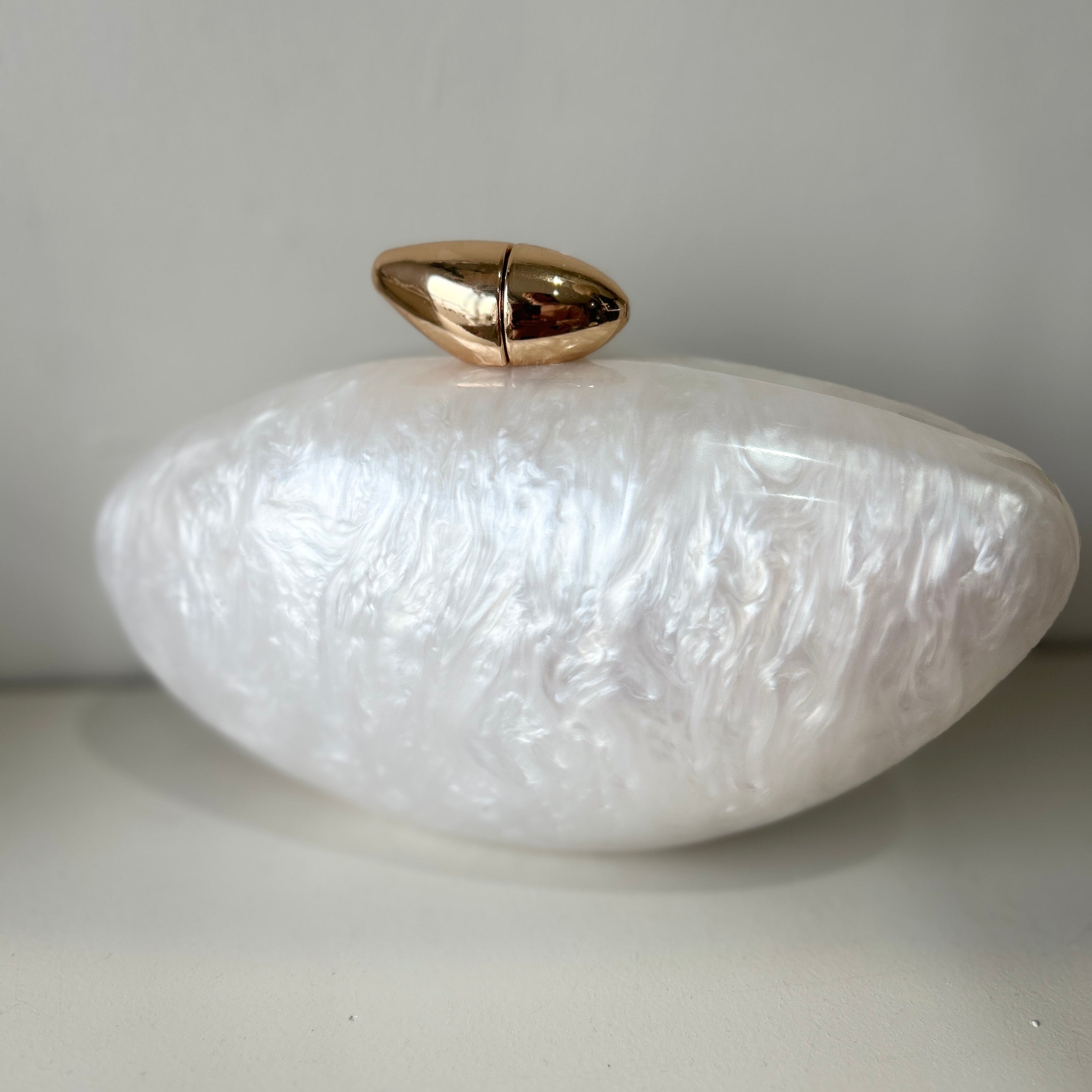 White textured clutch with gold accent on a light gray background