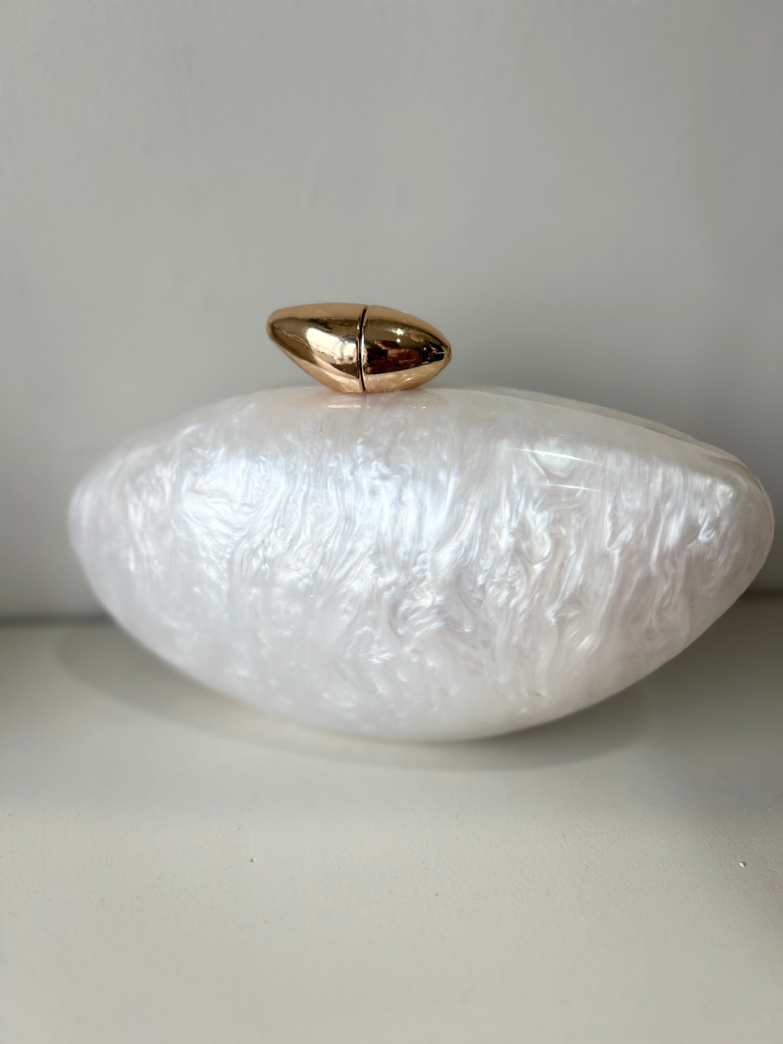 White textured clutch with gold accent on a light gray background