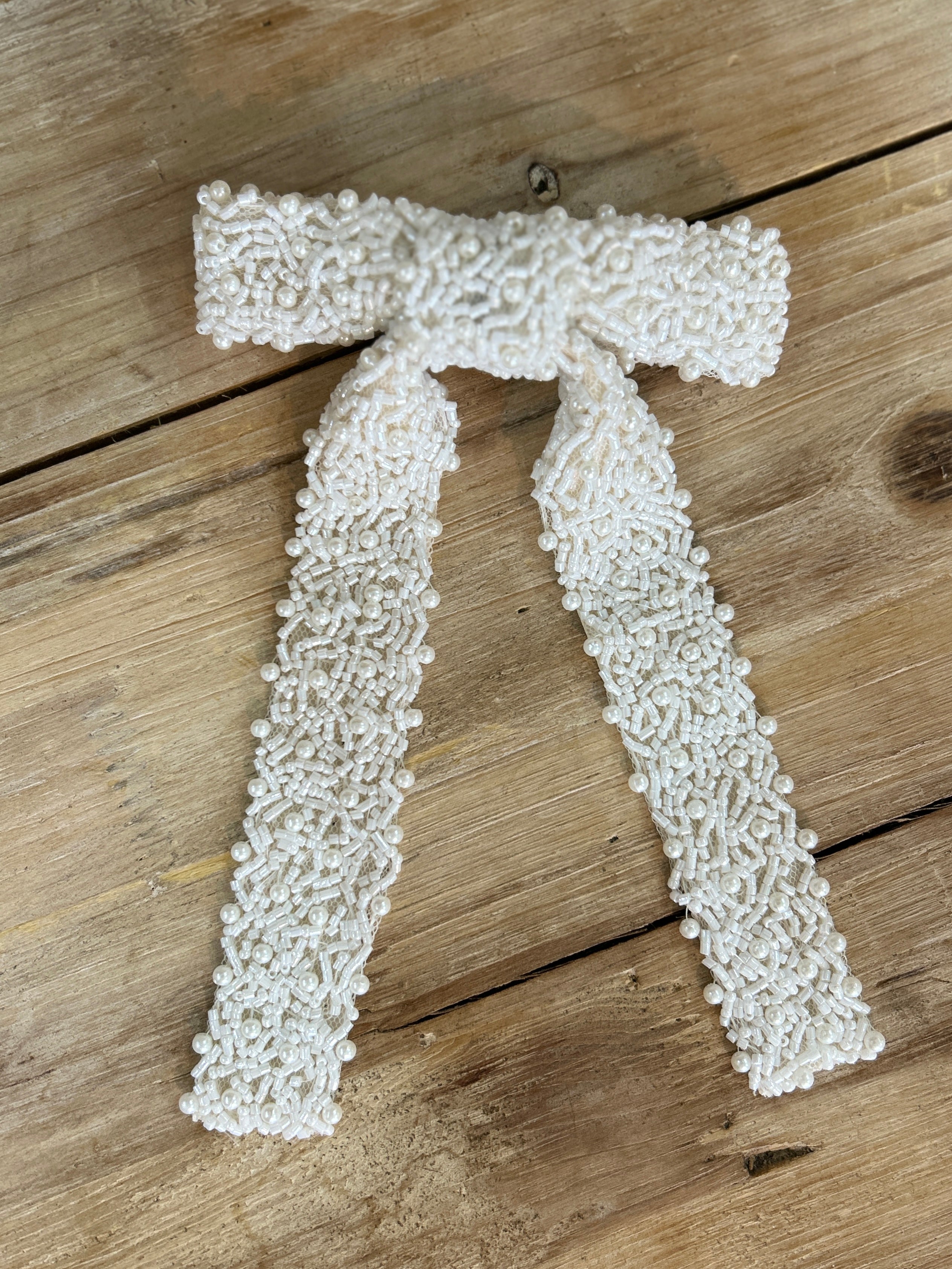White beaded bridal hair bow on a wooden surface