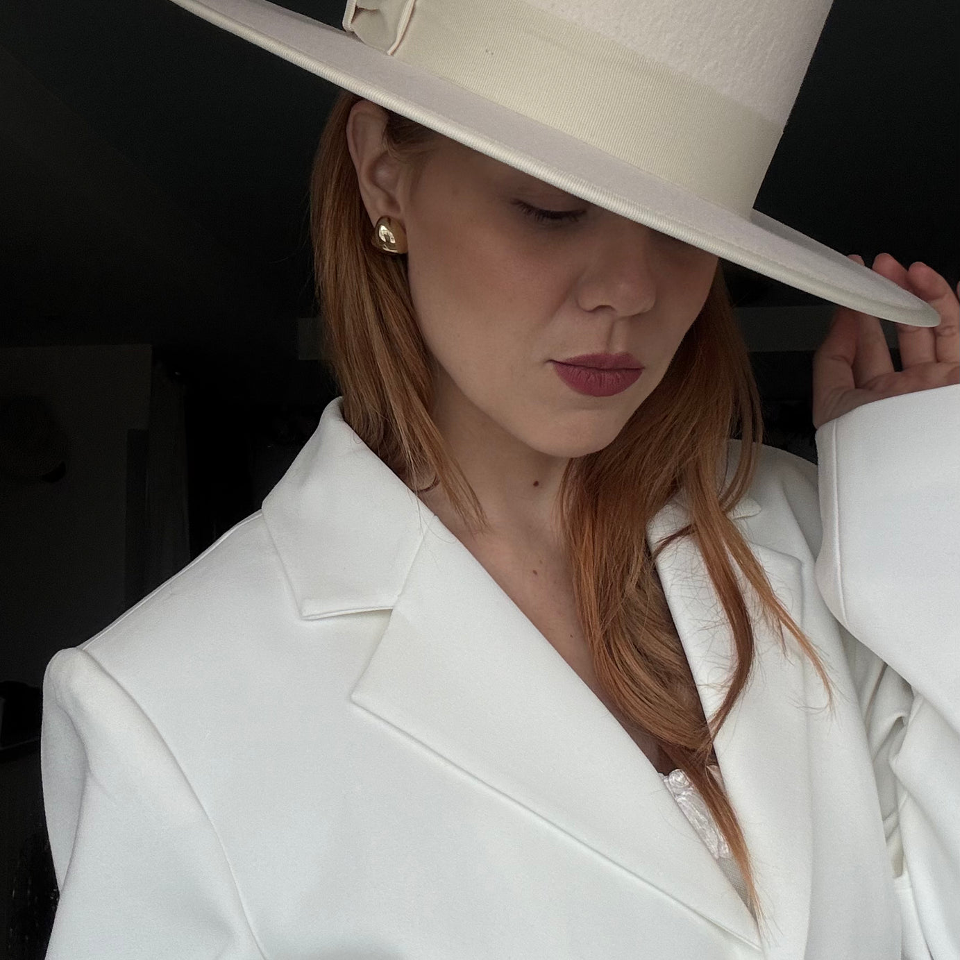 Woman wearing a white hat and coat against a dark background