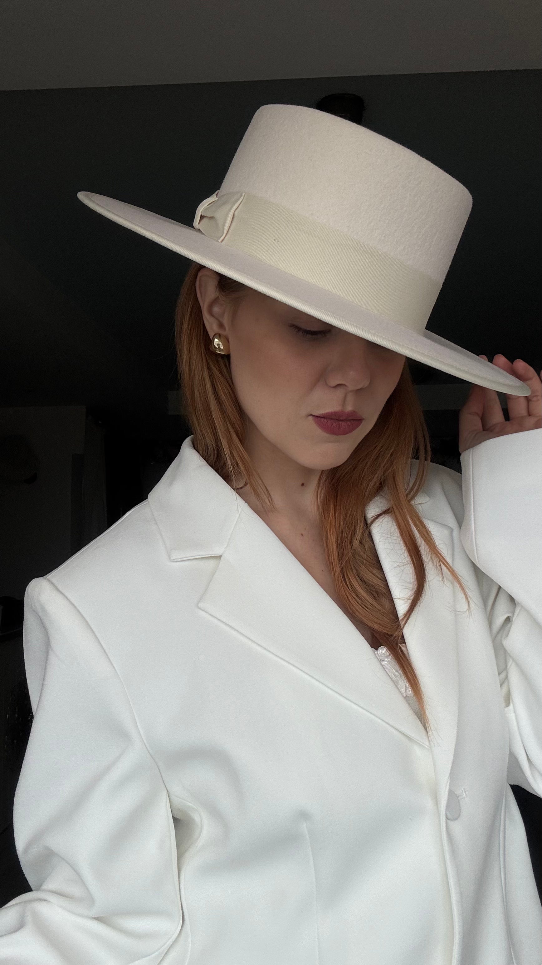 Woman wearing a white hat and coat against a dark background