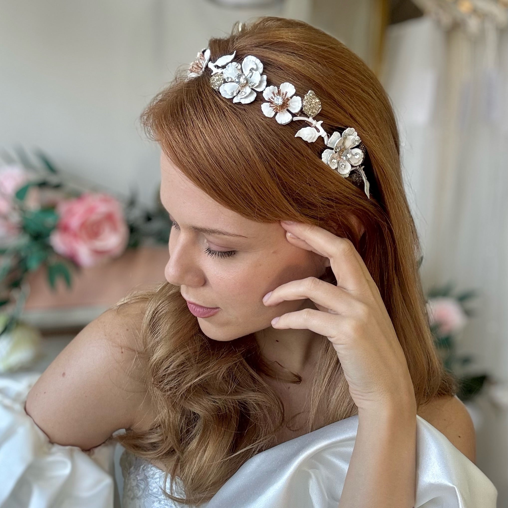 Woman wearing a decorative headband with flowers and leaves, with a blurred floral background.