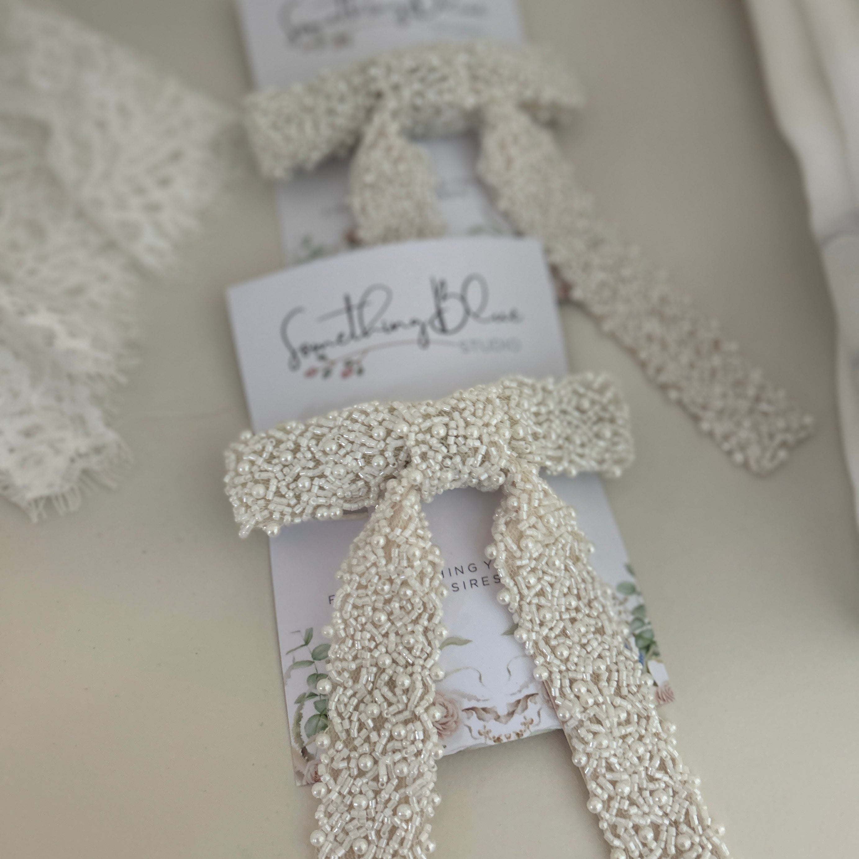 Set of White beaded bridal hair bows on beige background with 'Something Blue' card.