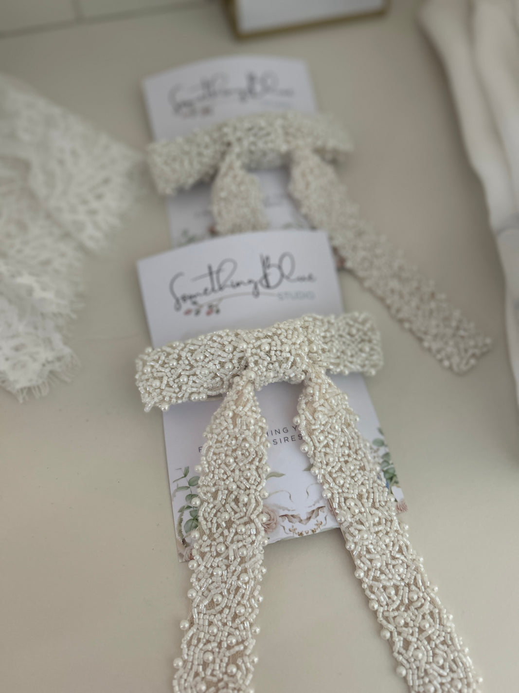 Set of White beaded bridal hair bows on beige background with 'Something Blue' card.
