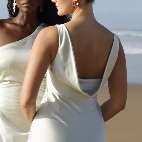 Two women in pastel green satin dresses standing on a beach.