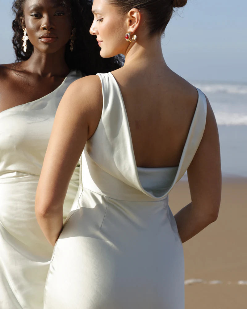 Two women in pastel green satin dresses standing on a beach.