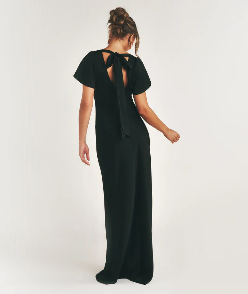 Woman wearing a black bridesmaid dress with a bow detail on a white background