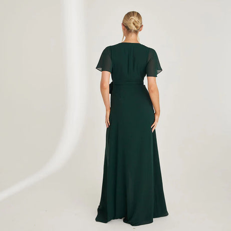 Woman wearing an emerald green chiffon gown with ruffled shoulders on a white background