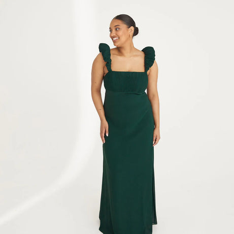 Woman wearing an emerald green chiffon gown with ruffled shoulders on a white background