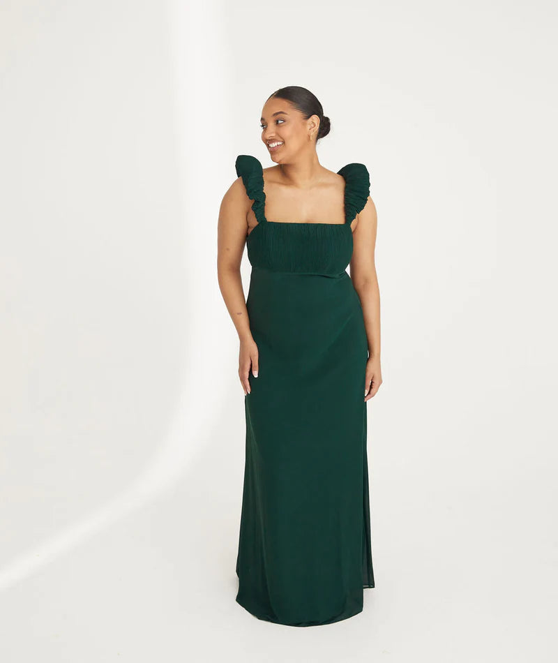 Woman wearing an emerald green chiffon gown with ruffled shoulders on a white background