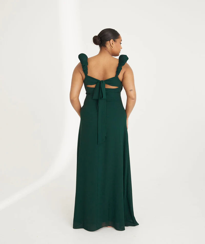 Woman wearing an emerald green chiffon gown with ruffled shoulders on a white background