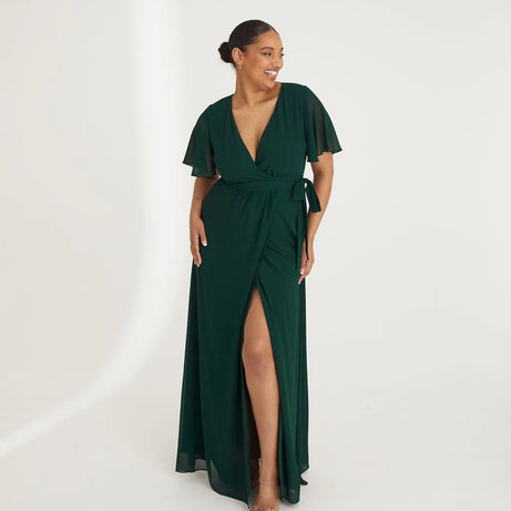Woman wearing an emerald green chiffon gown with ruffled shoulders on a white background