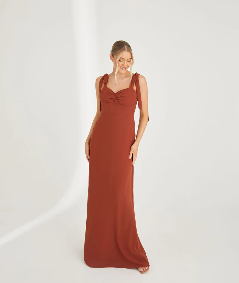 Woman wearing a rust-colored chiffon bridesmaid dress on a white background