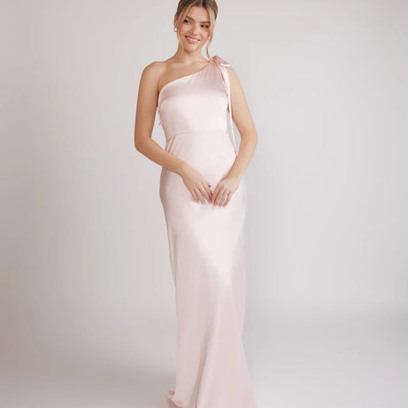 Woman wearing a one-shoulder light pink bridesmaid dress against a plain background