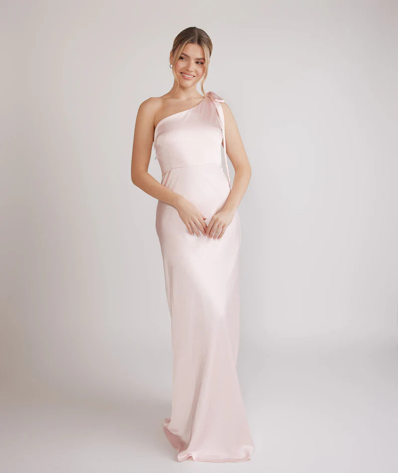 Woman wearing a one-shoulder light pink bridesmaid dress against a plain background