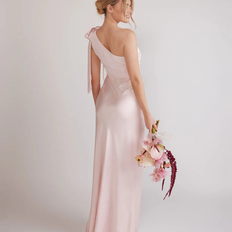 Woman wearing a one-shoulder light pink bridesmaid dress against a plain background