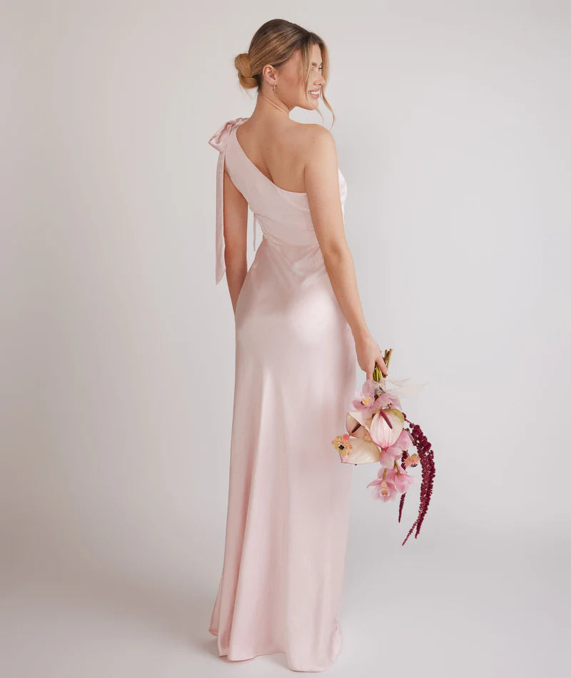 Woman wearing a one-shoulder light pink bridesmaid dress against a plain background