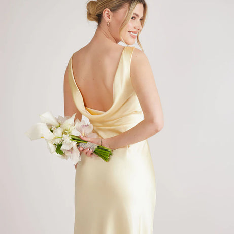 woman wearing lemon satin bridesmaid dress with cowl back against white background