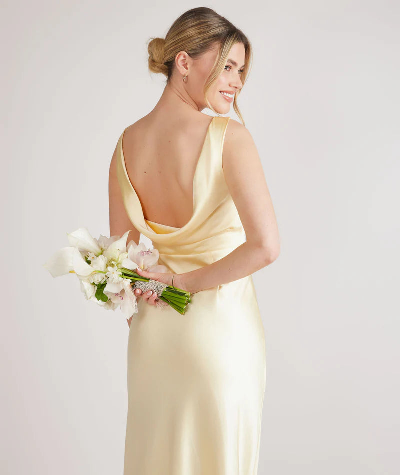 woman wearing lemon satin bridesmaid dress with cowl back against white background